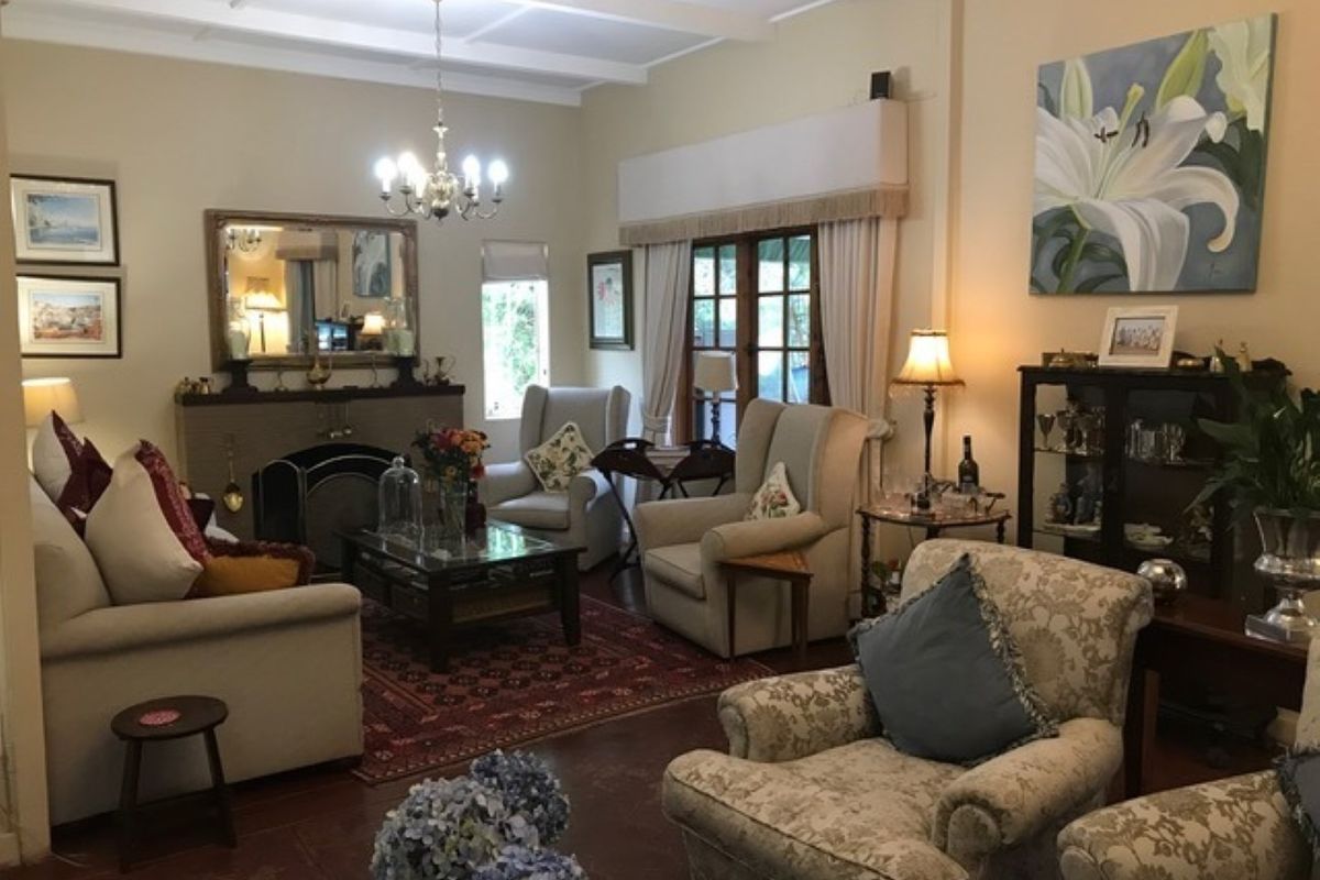 A cozy living room featuring a traditional fireplace, exposed beam ceiling, and timber flooring, with direct access to the garden through french doors.