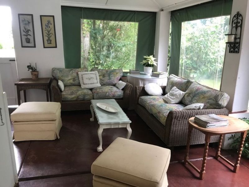 A covered, enclosed patio area featuring concrete flooring and roll-up weather blinds, providing a comfortable transition space to the garden.