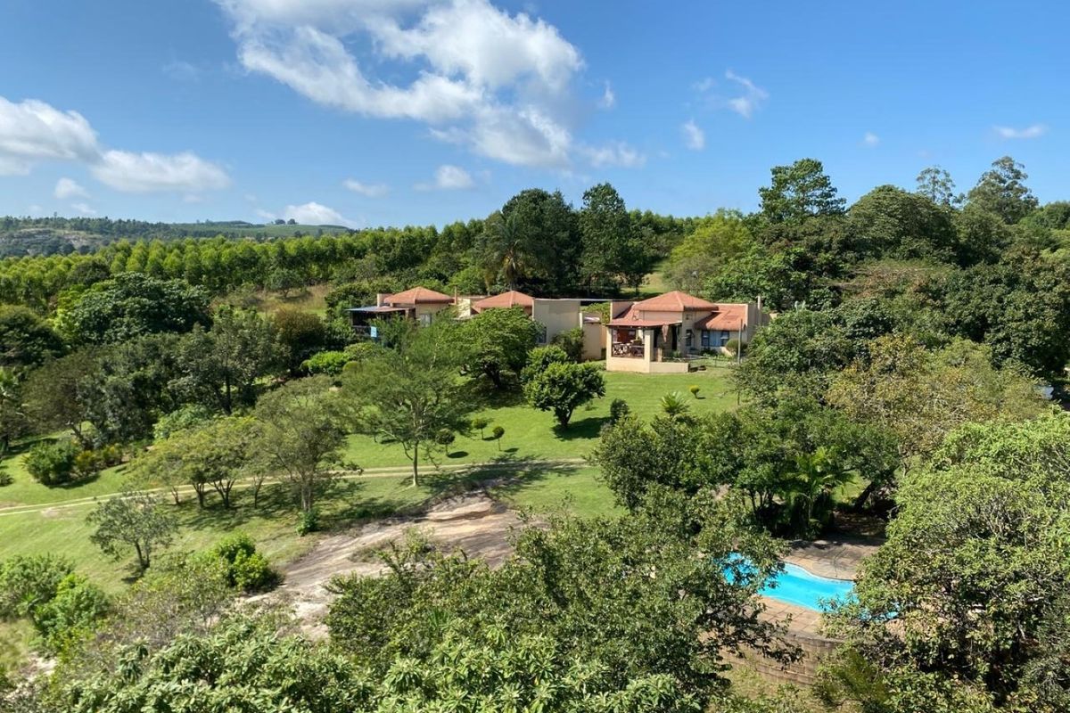 An aerial view of the farm property featuring a swimming pool, lush landscaped gardens, and multiple residential buildings with tiled roofs.
