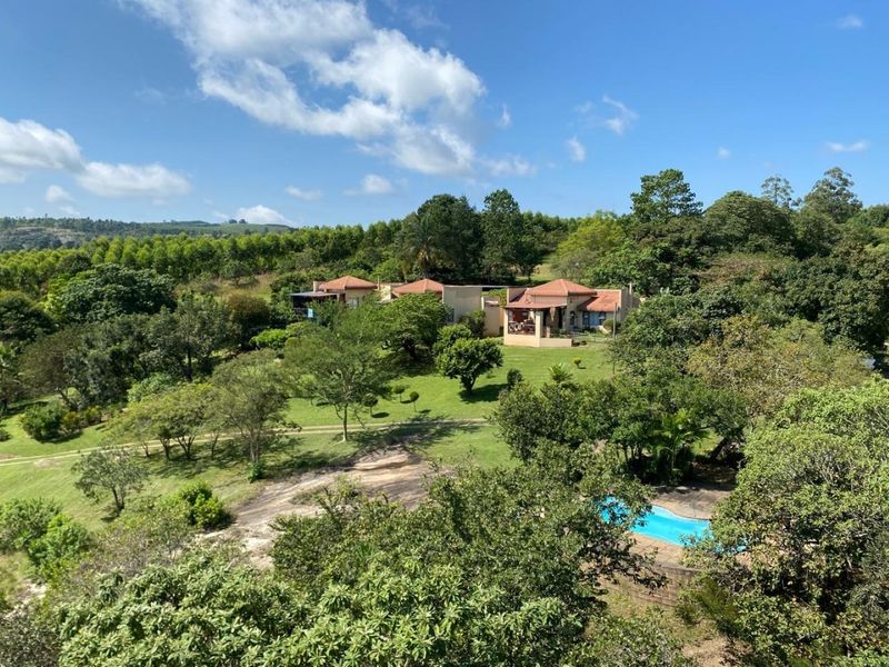 An aerial view of the farm property featuring a swimming pool, lush landscaped gardens, and multiple residential buildings with tiled roofs.