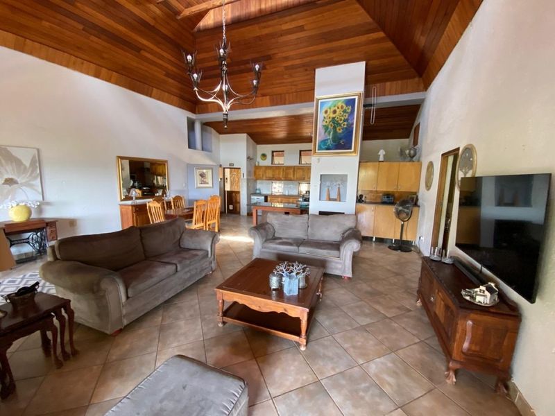 Spacious open-plan living and kitchen area featuring a high vaulted timber ceiling, tiled floors, and a central fireplace, offering a warm and rustic atmosphere.