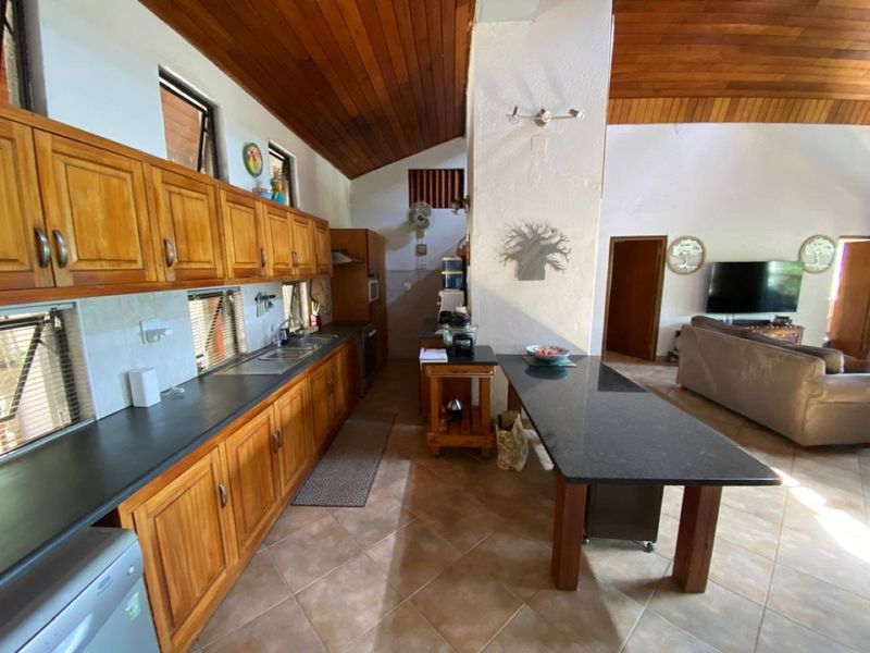 Open-plan kitchen and living area featuring timber vaulted ceilings, wooden cabinetry, granite countertops, and tiled flooring in a functional farm-style layout.