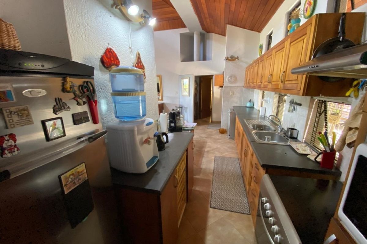 A functional kitchen featuring wooden cabinetry, double basin sink, extractor fan, and exposed timber ceilings, offering a warm and practical workspace.