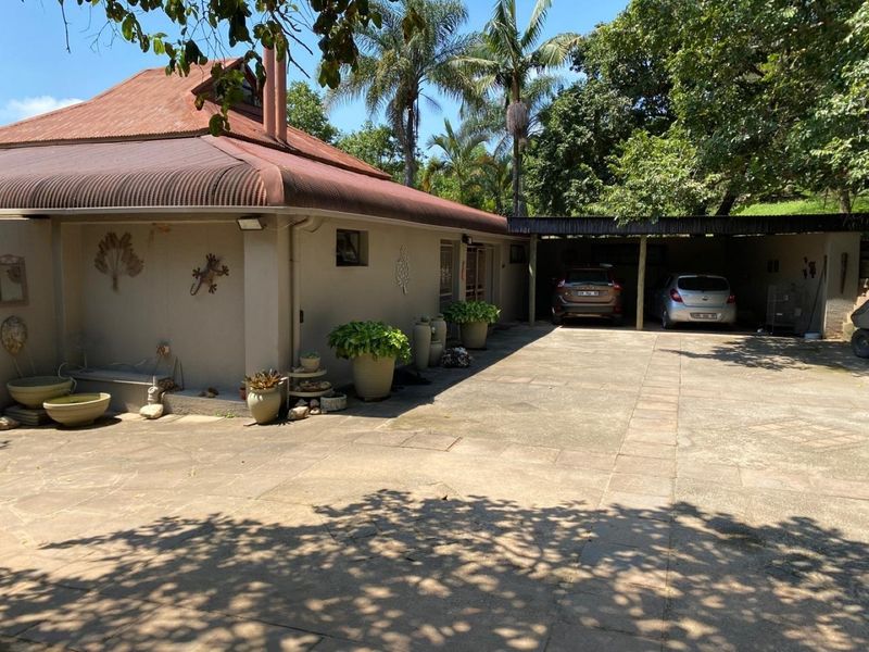 Front exterior view of the farm property featuring a paved driveway, carport, and a corrugated metal roof structure.