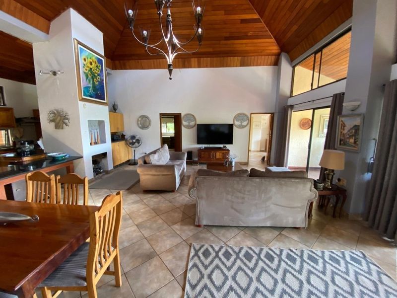 Spacious open-plan living and dining area featuring a high vaulted timber ceiling, tiled floors, and a built-in fireplace with direct access to outdoor space.