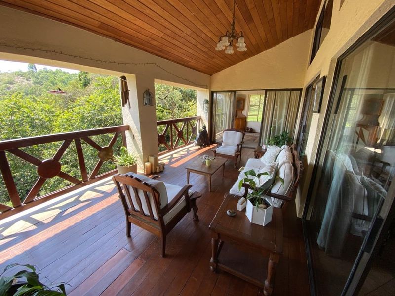 A spacious covered patio featuring timber decking, a vaulted timber ceiling, and a wooden balustrade, offering scenic views of the surrounding landscape.