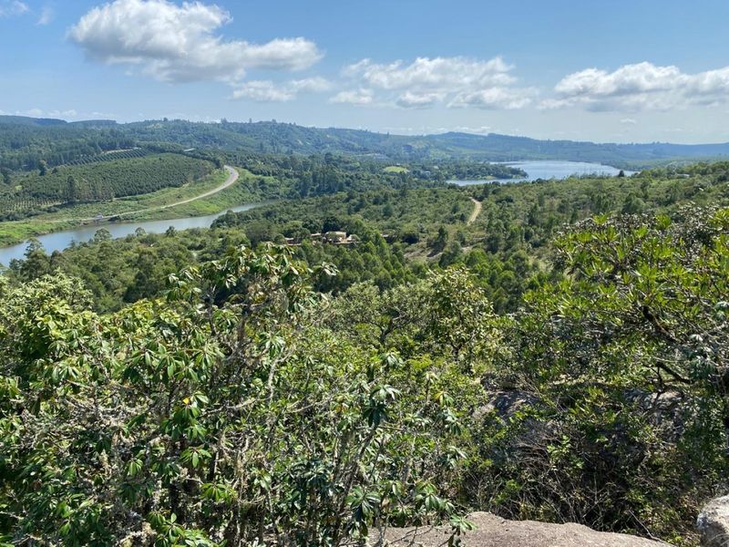 A scenic elevated landscape view overlooking lush green hills, dense forest, and a tranquil river winding through the countryside.