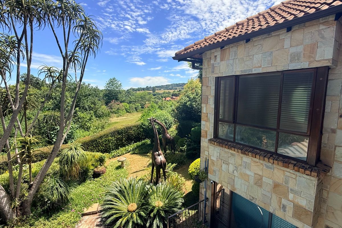 A view of the rear elevation featuring natural stone cladding, tiled roofing, and large windows overlooking a lush garden and landscape.