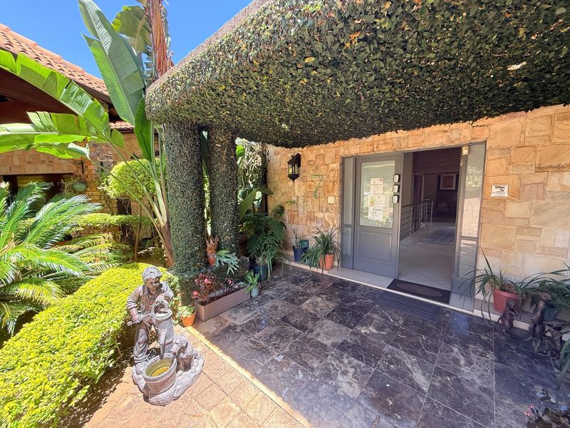 Inviting front entrance featuring natural stone cladding, a lush ivy-covered pergola, and dark tiled flooring leading into the main residence.