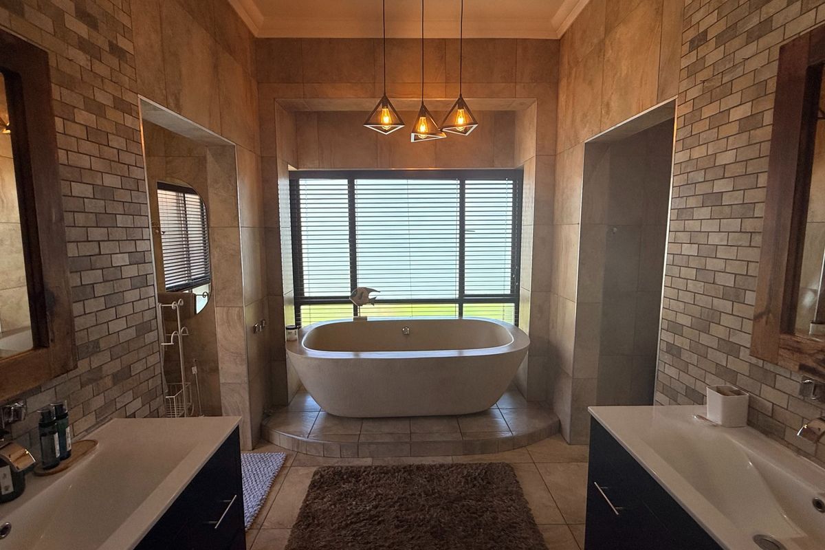 Modern bathroom featuring a central freestanding bathtub, double vanity with integrated sinks, and elegant tiled finishes with warm pendant lighting.