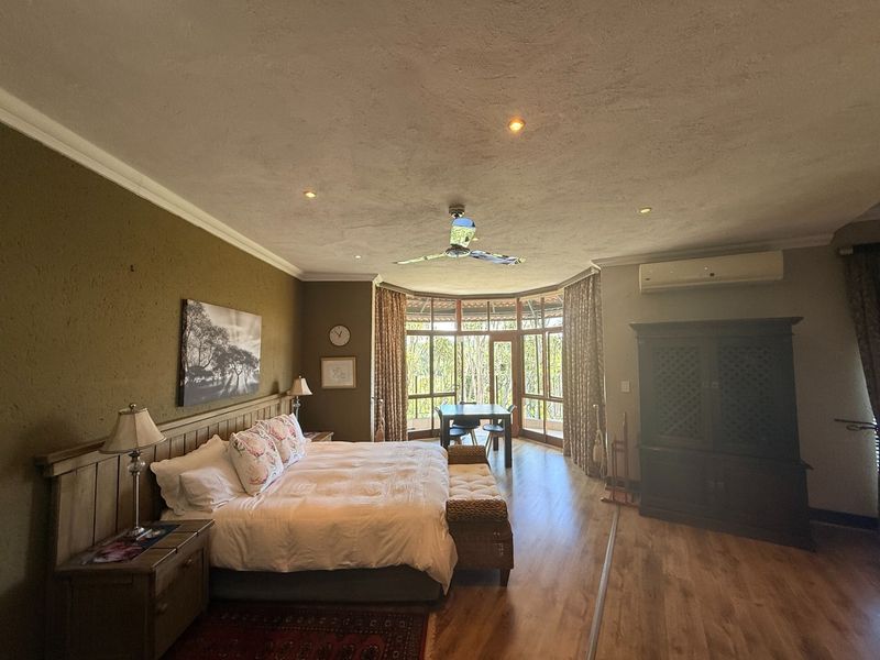 Spacious bedroom featuring laminate flooring, recessed lighting, a ceiling fan, split-system air conditioning, and large timber-framed windows with garden views.