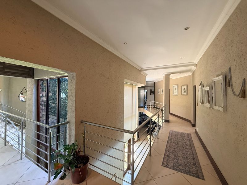 Spacious upper-level hallway featuring tiled flooring, stainless steel balustrades overlooking the lower level, and recessed ceiling lighting.