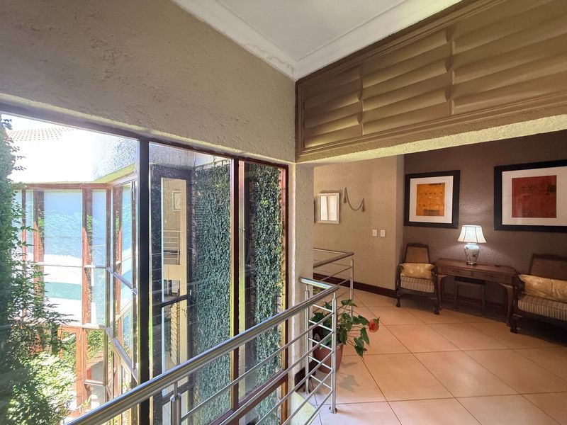 Spacious hallway featuring tiled flooring, a modern stainless steel balustrade, and large windows overlooking an internal courtyard with greenery.