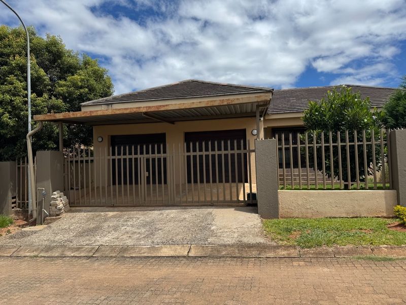Front elevation of a house featuring a double garage, attached carport, and secure perimeter fencing with a paved driveway.
