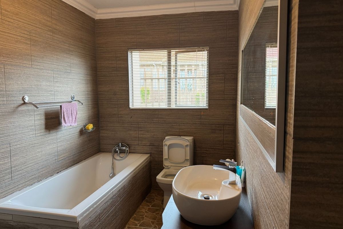 A modern bathroom featuring full-height textured wall tiling, a built-in bathtub, a vessel sink vanity, and a wall-mounted toilet.