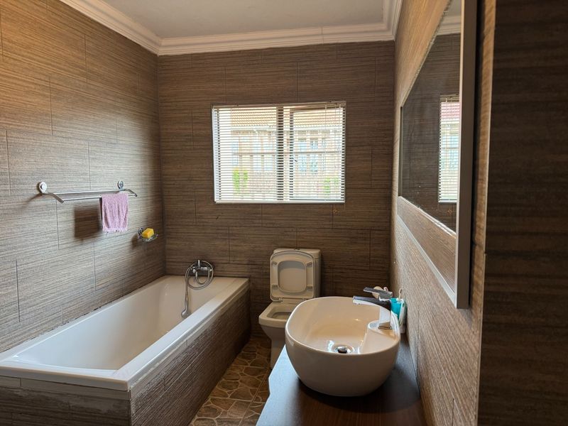 A modern bathroom featuring full-height textured wall tiling, a built-in bathtub, a vessel sink vanity, and a wall-mounted toilet.