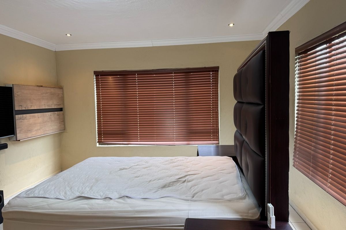 A well-maintained bedroom featuring tiled flooring, recessed downlighting, crown molding, and wooden venetian blinds.