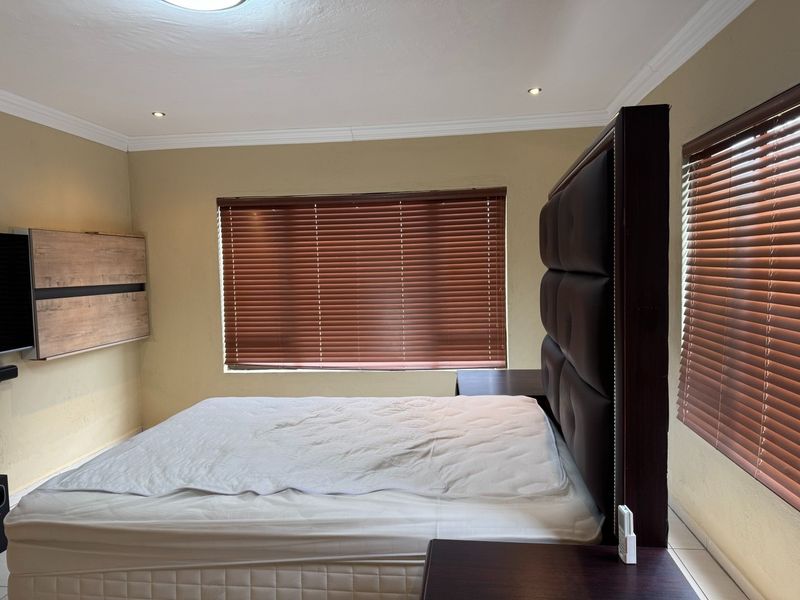 A well-maintained bedroom featuring tiled flooring, recessed downlighting, crown molding, and wooden venetian blinds.