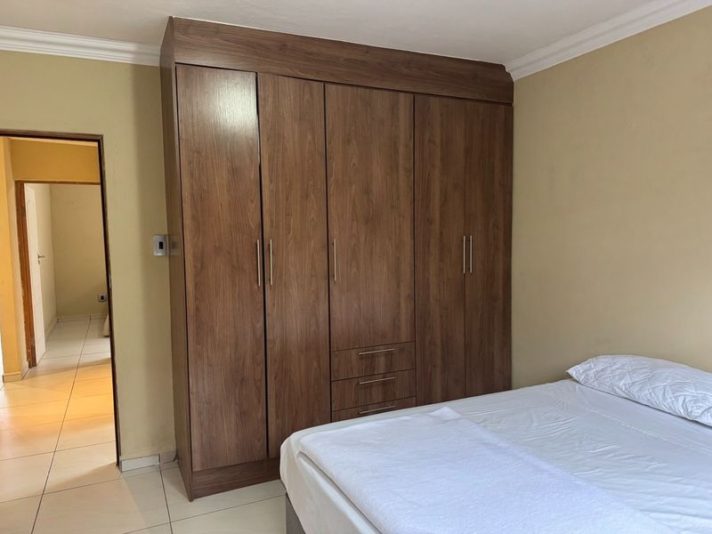 A bedroom featuring a large, modern wood-finish built-in wardrobe with integrated drawers and tiled flooring.