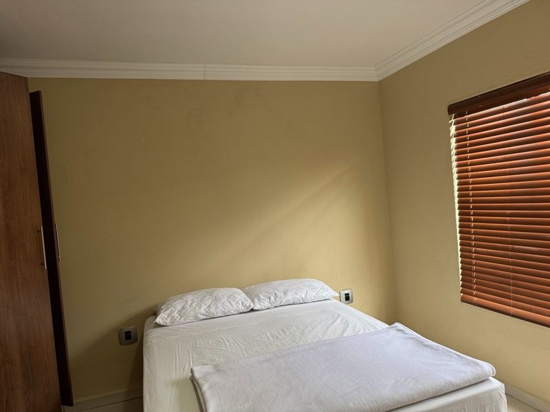 A functional bedroom featuring a built-in wardrobe, crown molding, and wooden venetian blinds, providing a neutral base for personalization.
