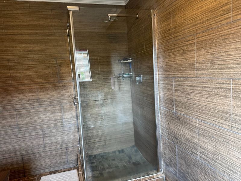 A modern walk-in shower featuring a glass enclosure, rain shower head, and textured wood-look wall tiling.