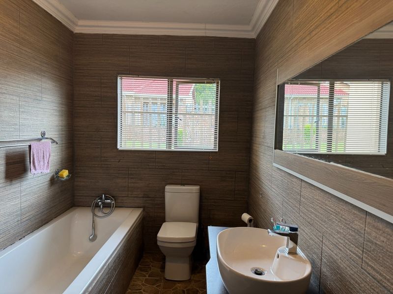 A modern bathroom featuring wood-look wall tiles, a vessel sink vanity, a built-in bathtub, and a toilet.