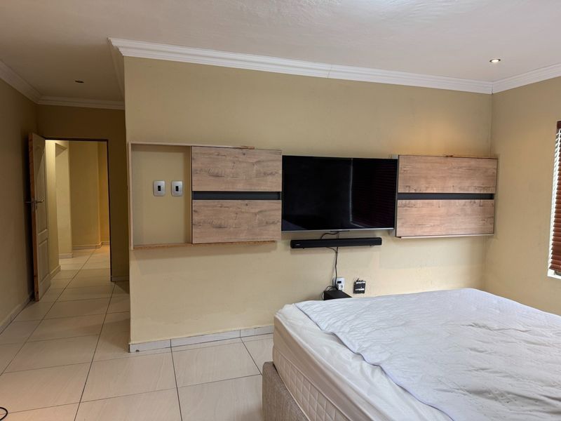 Bedroom featuring tiled flooring, recessed downlights, and a built-in wall unit with integrated shelving and television mounting space.