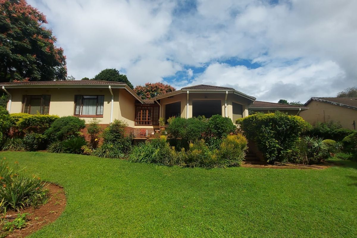 A view of the rear elevation of the house featuring a tiled roof, brick foundation, and a well-maintained landscaped garden with a patio area.