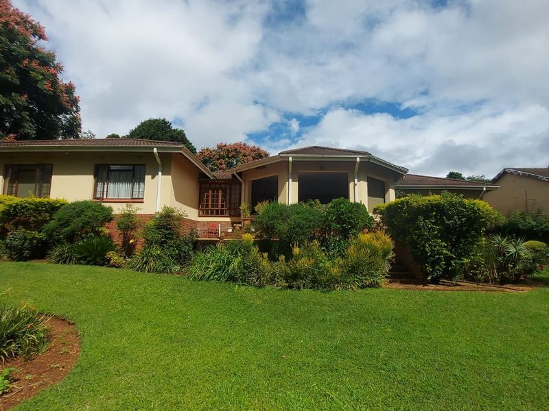 A view of the rear elevation of the house featuring a tiled roof, brick foundation, and a well-maintained landscaped garden with a patio area.