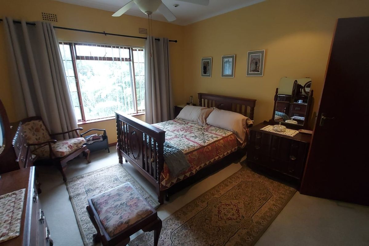A well-proportioned bedroom featuring a ceiling fan and large window with security bars, offering a functional space with neutral wall tones.
