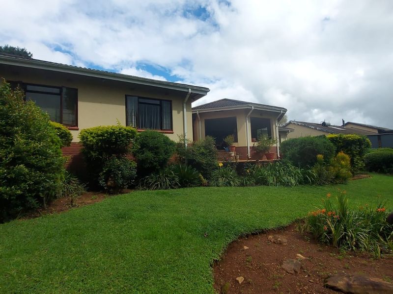 A view of the rear elevation of the house featuring a covered patio area, established garden, and well-maintained brick and plaster exterior finishes.