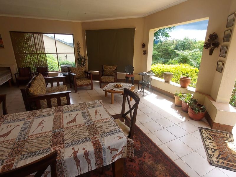 A spacious covered patio featuring tiled flooring and large windows, offering a bright and airy transition to the garden area.