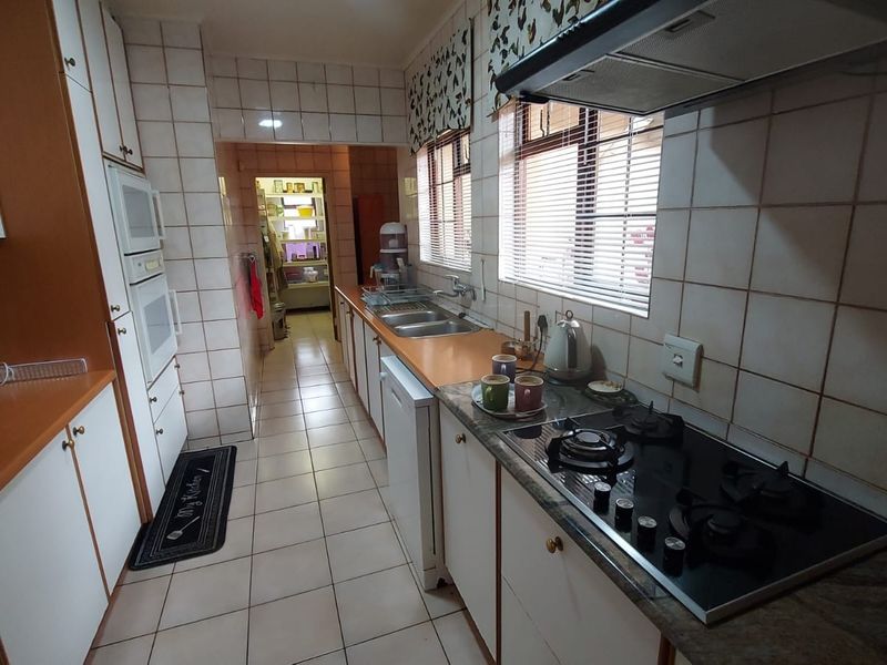 A functional kitchen featuring built-in cabinetry, a gas hob with extractor fan, built-in oven, and tiled finishes throughout.
