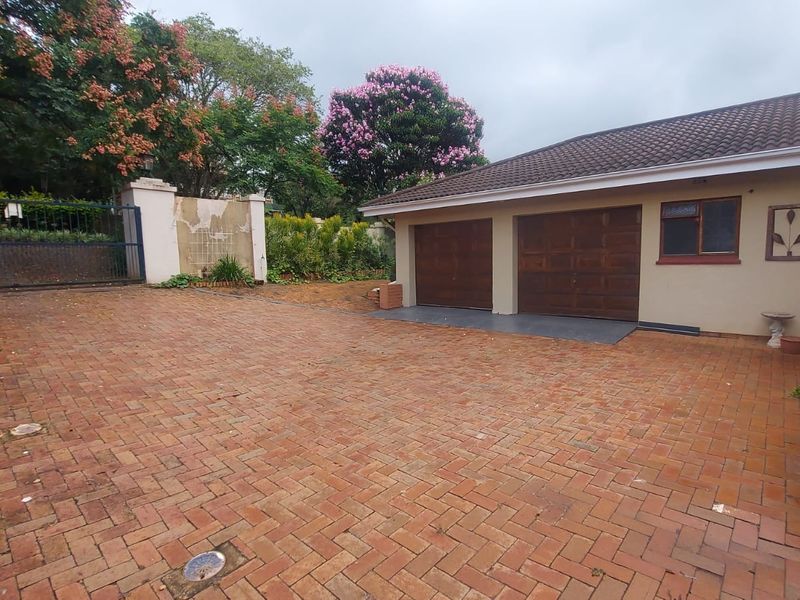 Front exterior view featuring a brick paved driveway, double garage with wooden doors, and a perimeter wall with gated access.