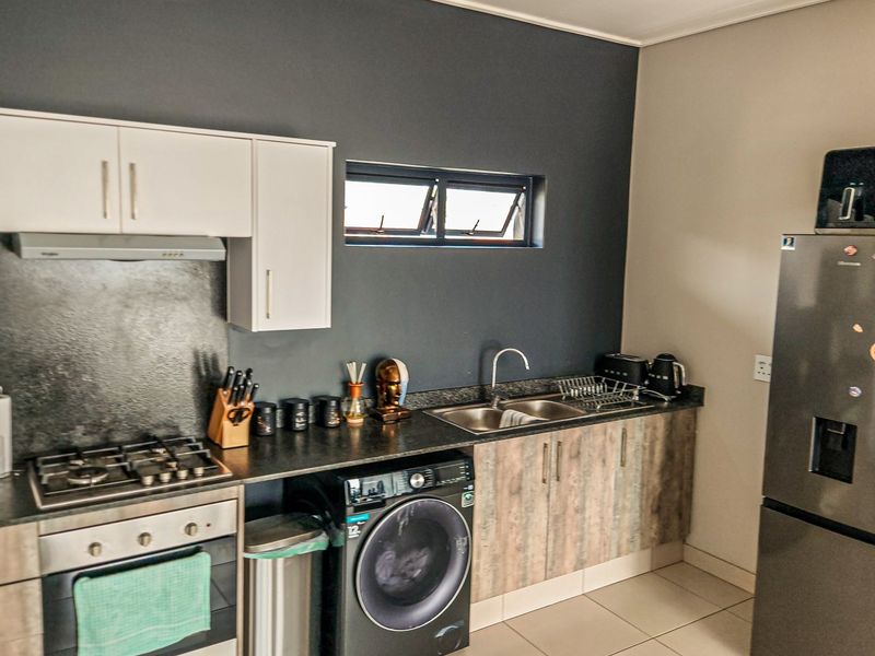 Modern kitchen featuring dark accent walls, laminate cabinetry, gas hob, built-in oven, and tiled flooring with integrated laundry appliance space.