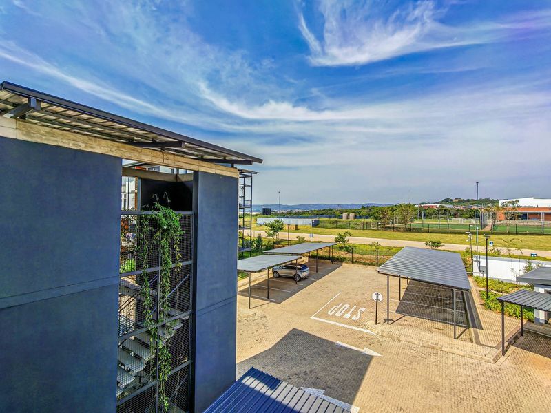 Elevated view of the apartment complex exterior, featuring paved parking areas with covered bays and a modern stairwell structure.
