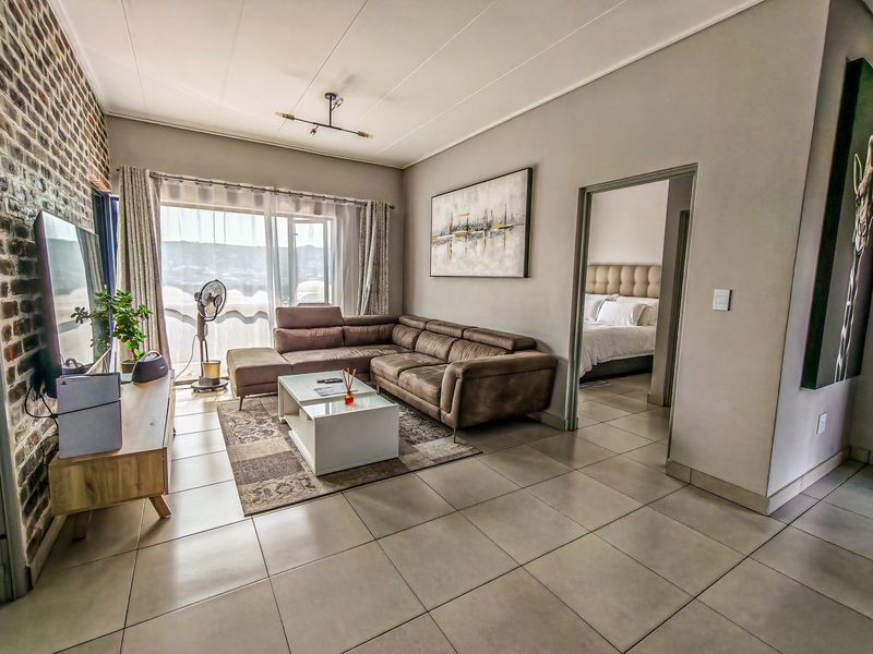 Spacious living room featuring tiled floors, an exposed brick feature wall, and large sliding doors leading to an outdoor area.