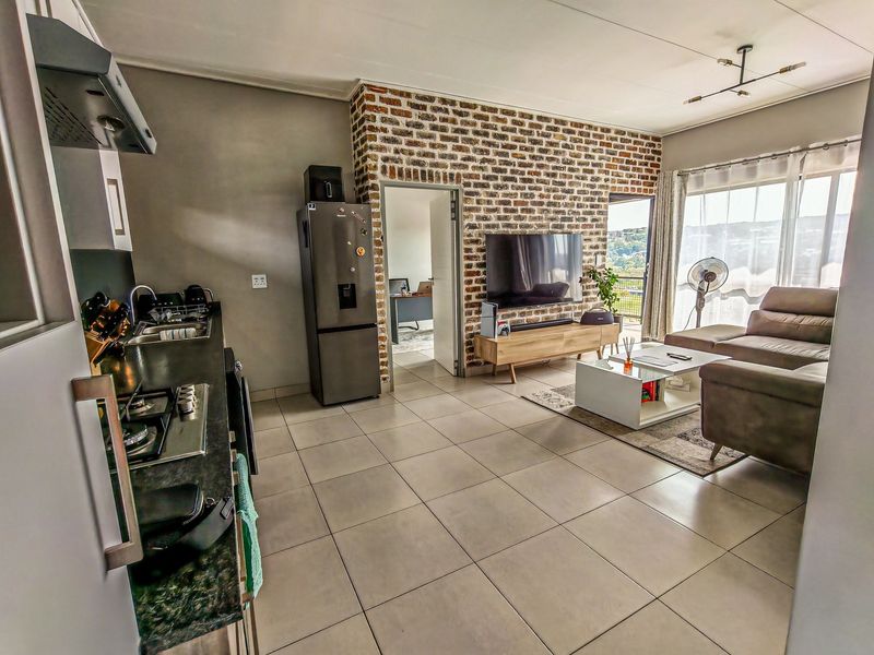 Open-plan living area featuring a modern kitchen with gas hob, tiled floors, and an exposed brick feature wall leading to a balcony.