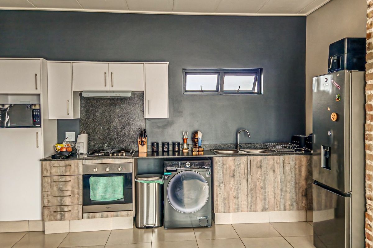 Modern kitchen featuring built-in oven, gas hob, extractor fan, integrated microwave, and ample cabinetry with stone countertops and tiled flooring.