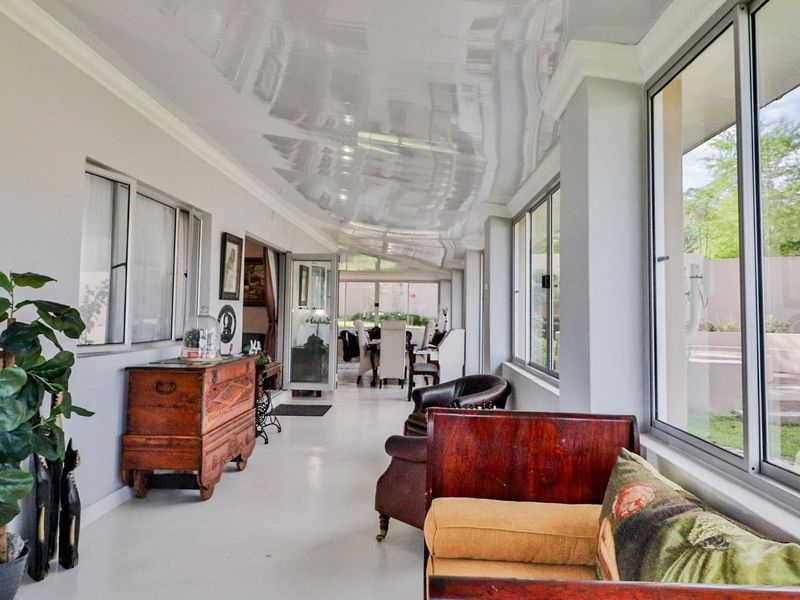 A bright, enclosed patio featuring large aluminium sliding windows, a reflective stretch ceiling, and neutral tiled flooring, offering a seamless transition to the garden.