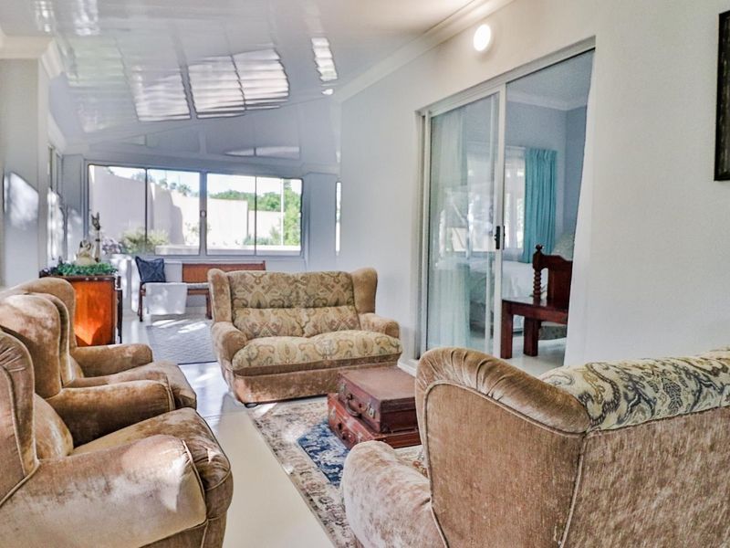 A bright, enclosed patio area featuring large glass windows, sliding doors, and tiled flooring, offering a versatile space for relaxation.