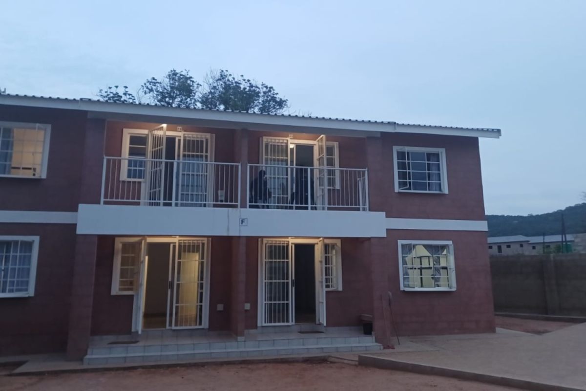 A two-story residential building featuring a brick facade, ground floor patio, and upper-level balcony with security gates and bars on all windows and doors.