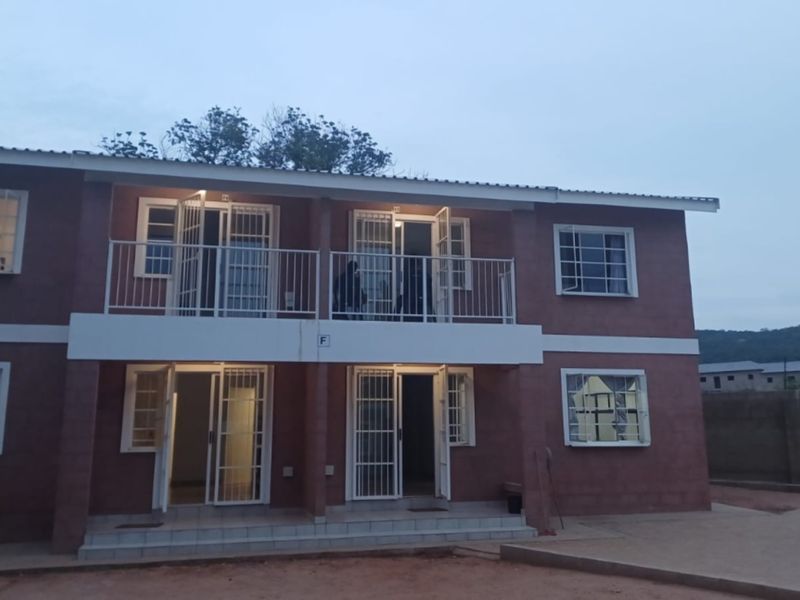 A two-story residential building featuring a brick facade, ground floor patio, and upper-level balcony with security gates and bars on all windows and doors.
