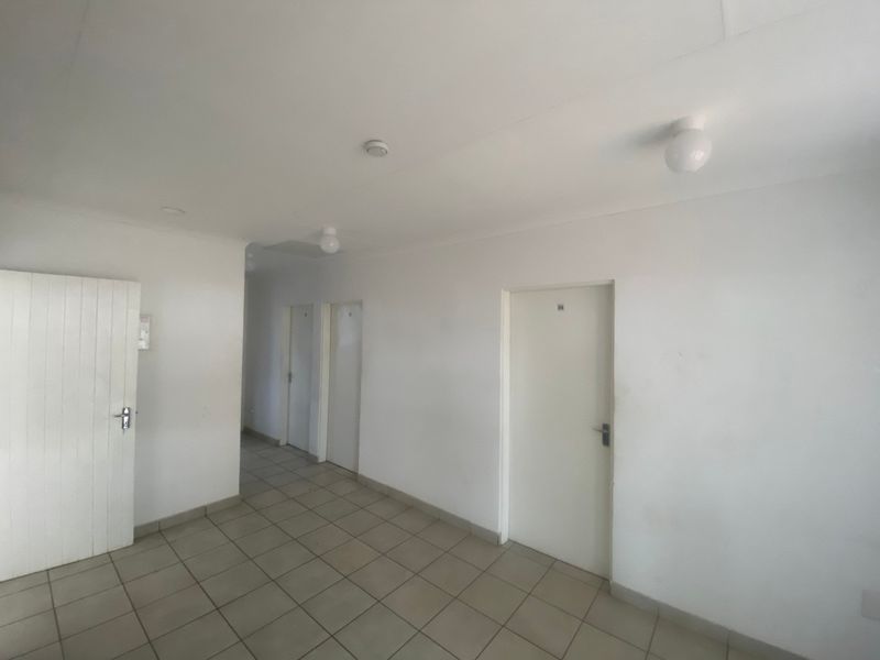 A vacant hallway featuring tiled flooring and multiple interior access points, presenting a blank canvas for potential interior design updates.