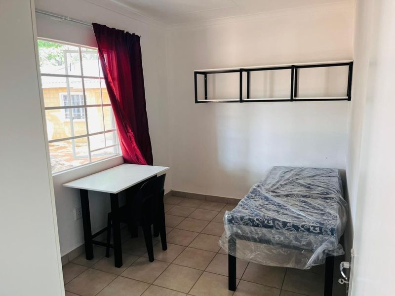 A simple bedroom featuring tiled flooring, a window with natural light, and wall-mounted shelving units.