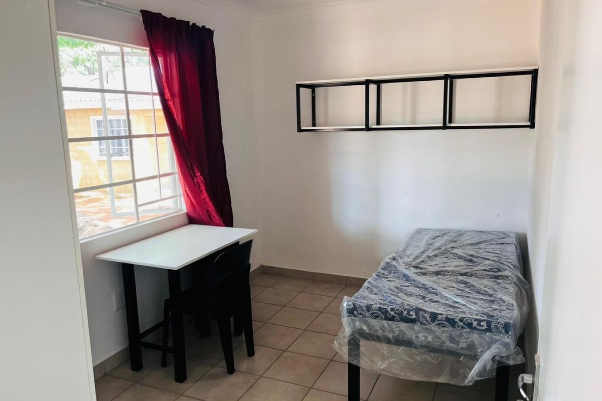 A simple bedroom featuring tiled flooring, a window with natural light, and wall-mounted shelving units.