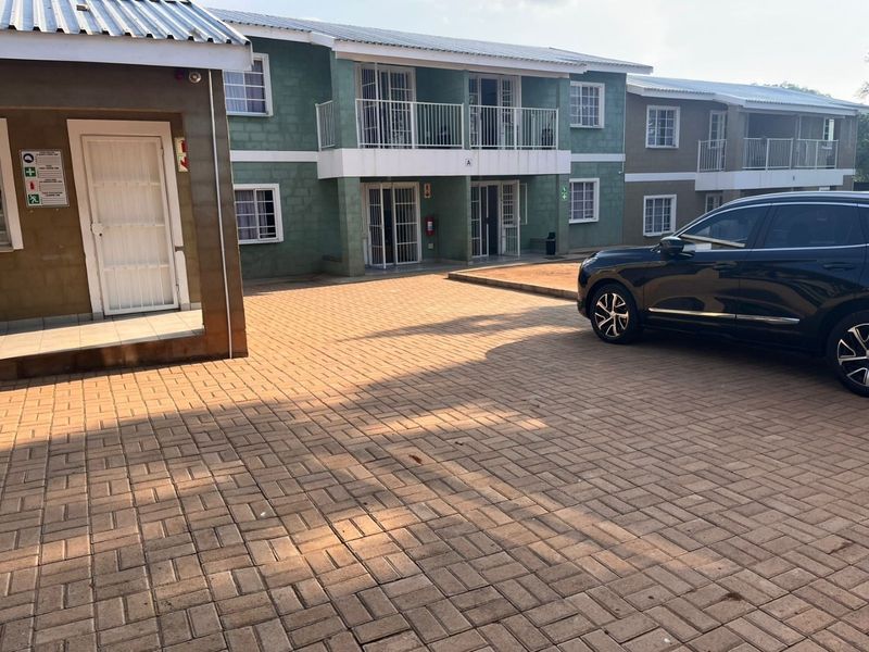 Exterior view of a multi-story residential complex featuring paved driveway access, ground floor entrances with security gates, and upper-level balconies.