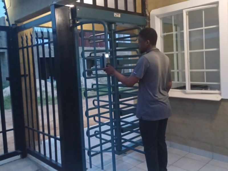 Exterior entrance area featuring a security turnstile, electric fencing, and tiled flooring at the property access point.