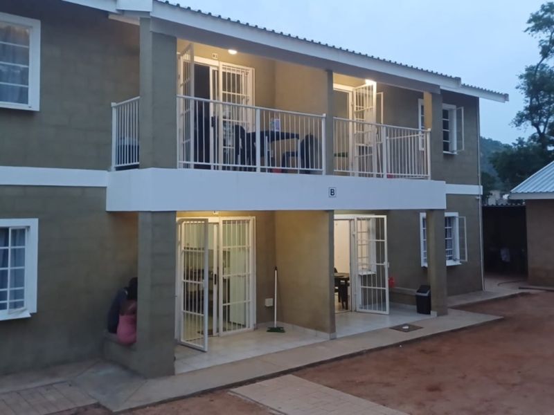 A two-story residential building featuring a ground-floor patio and an upper-level balcony with security gates and metal railings.