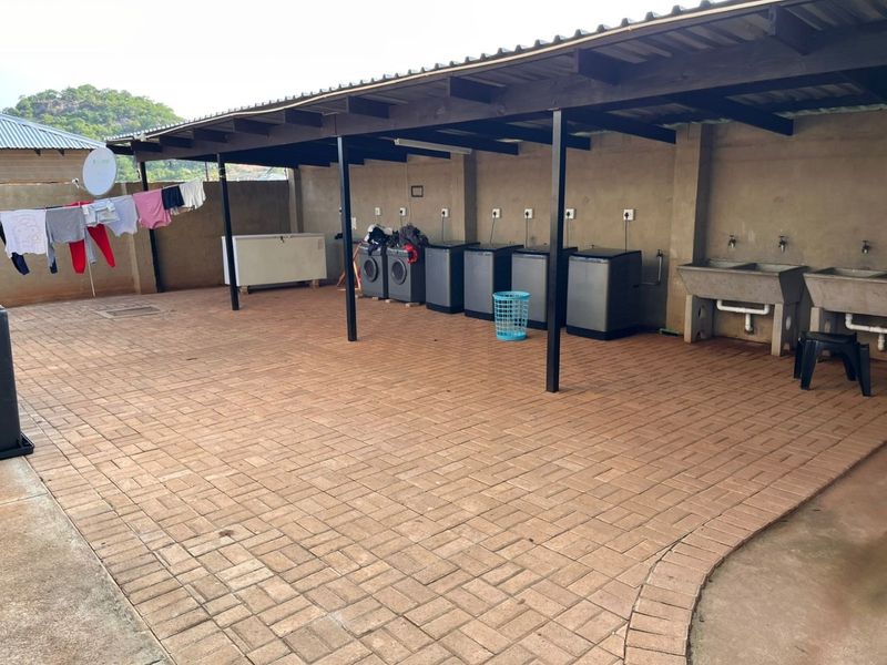 A spacious, covered outdoor laundry area featuring brick paving, multiple concrete wash basins, and dedicated plumbing connections for washing machines.